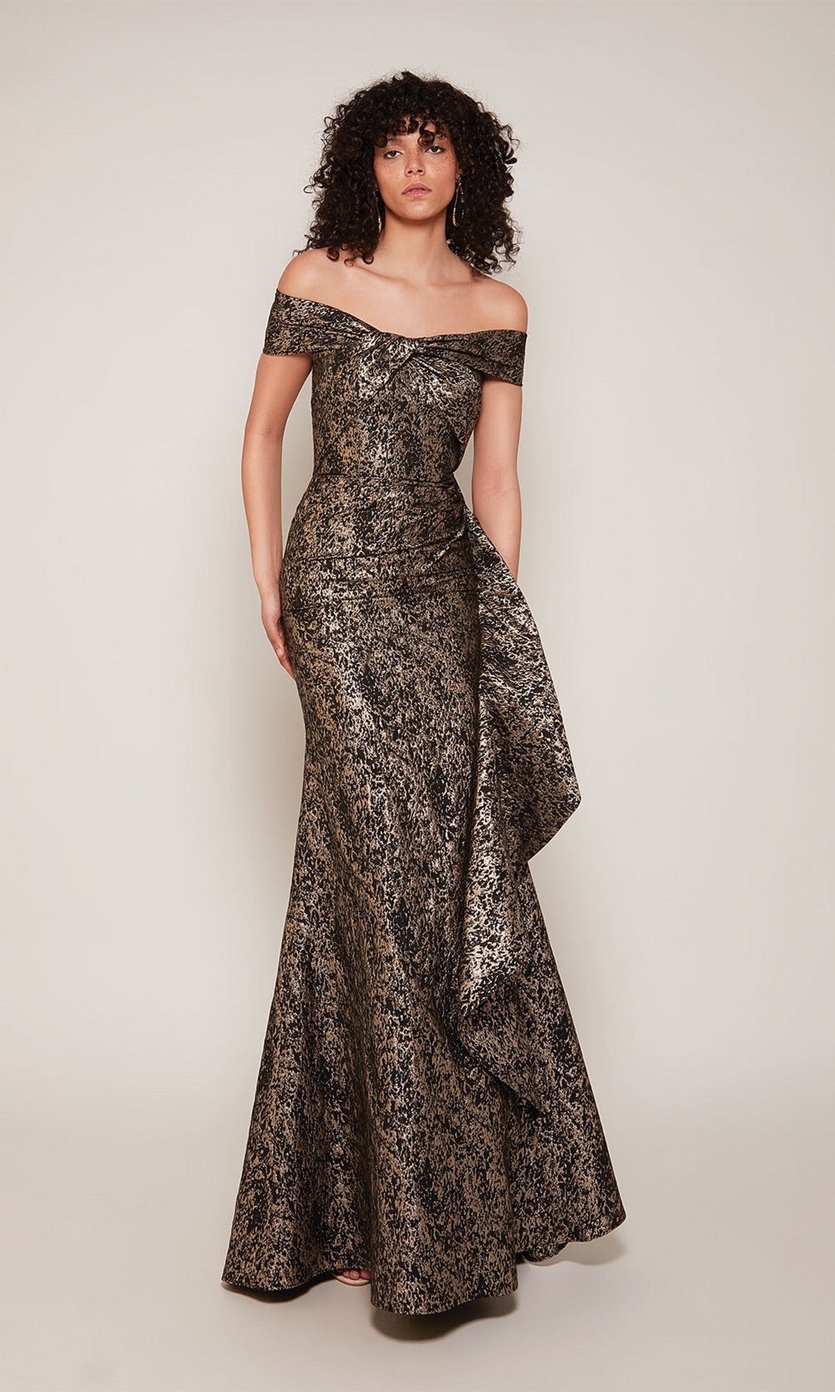 Woman modeling the Alyce 27667 long formal dress in mocha, a sophisticated off-the-shoulder, floor-length gown—perfect as a mother-of-the-bride look—standing against a plain light backdrop.
